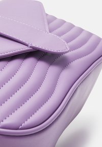 Borsa viola in similpelle con design trapuntato, dotata di chiusura a patta e cuciture a contrasto. Forma arrotondata con una texture liscia.