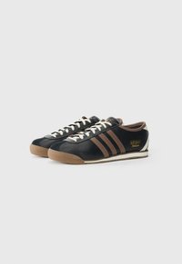 Sneakers in pelle nera con dettagli marroni, design a tre strisce, lacci bianchi e suola in gomma. Presentano un logo dorato sul lato.