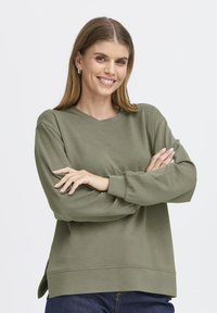 Sudadera verde oliva con un corte relajado, cuello redondo, puños acanalados y aberturas laterales. Textura suave con detalles de costura mínimos.