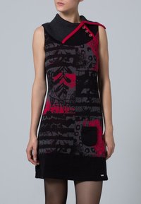 Ärmlös svart klänning med röda och grå abstrakta mönster, asymmetrisk krage med knappar, och en svart framficka.