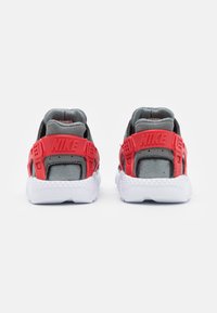 Nike sneakers pretos e vermelhos apresentam uma parte superior em malha cinza, suporte de calcanhar em plástico vermelho e sola de borracha texturizada branca, exibindo a vista traseira.