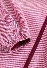 Tissu à motif vichy rose et blanc avec poignet élastique froncé et fermeture éclair rose foncé visible sur un vêtement.
