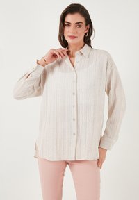 Cream textured long-sleeve shirt with a button-up front, pointed collar, and loose fit, paired with light pink pants.