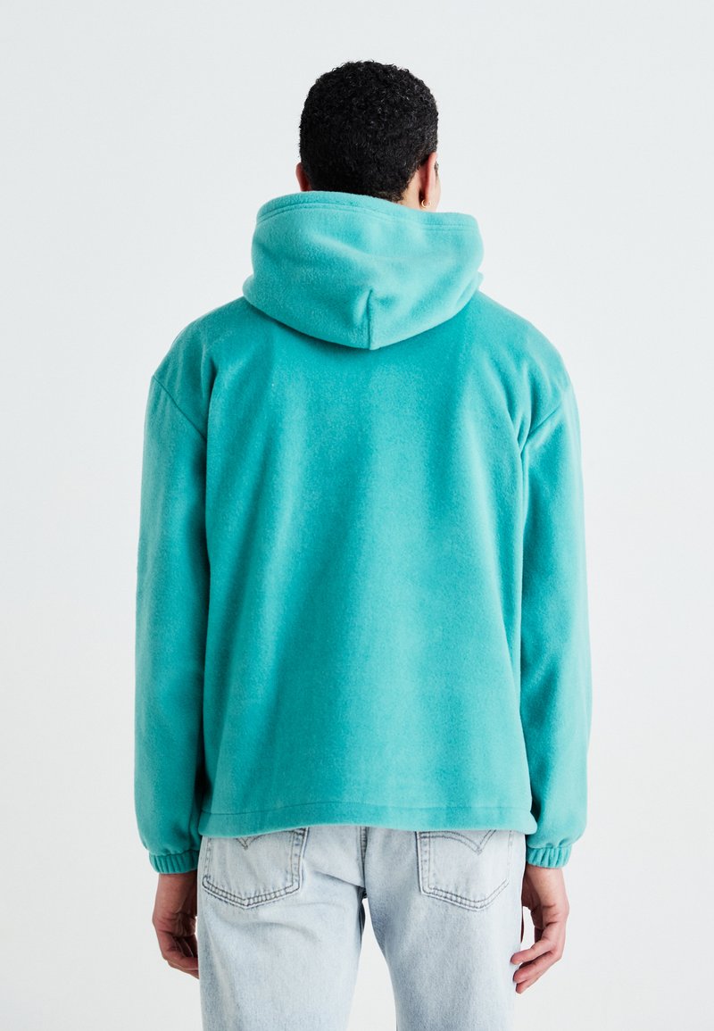 Türkisfarbener Fleece-Hoodie mit einer geräumigen Kapuze, elastischen Bündchen und einem lässigen Schnitt. Verfügt über eine glatte Textur und ein einfaches Design. Rückansicht gezeigt.