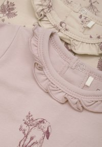 Set med två barnkläder med volangkragar. Den ena är ljusrosa med ett kaninmönster, den andra är beige med blommönster.