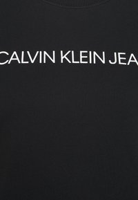 Felpa nera con texture a coste, caratterizzata dalla scritta "CALVIN KLEIN JEANS" stampata in lettere bianche in grassetto sul petto.