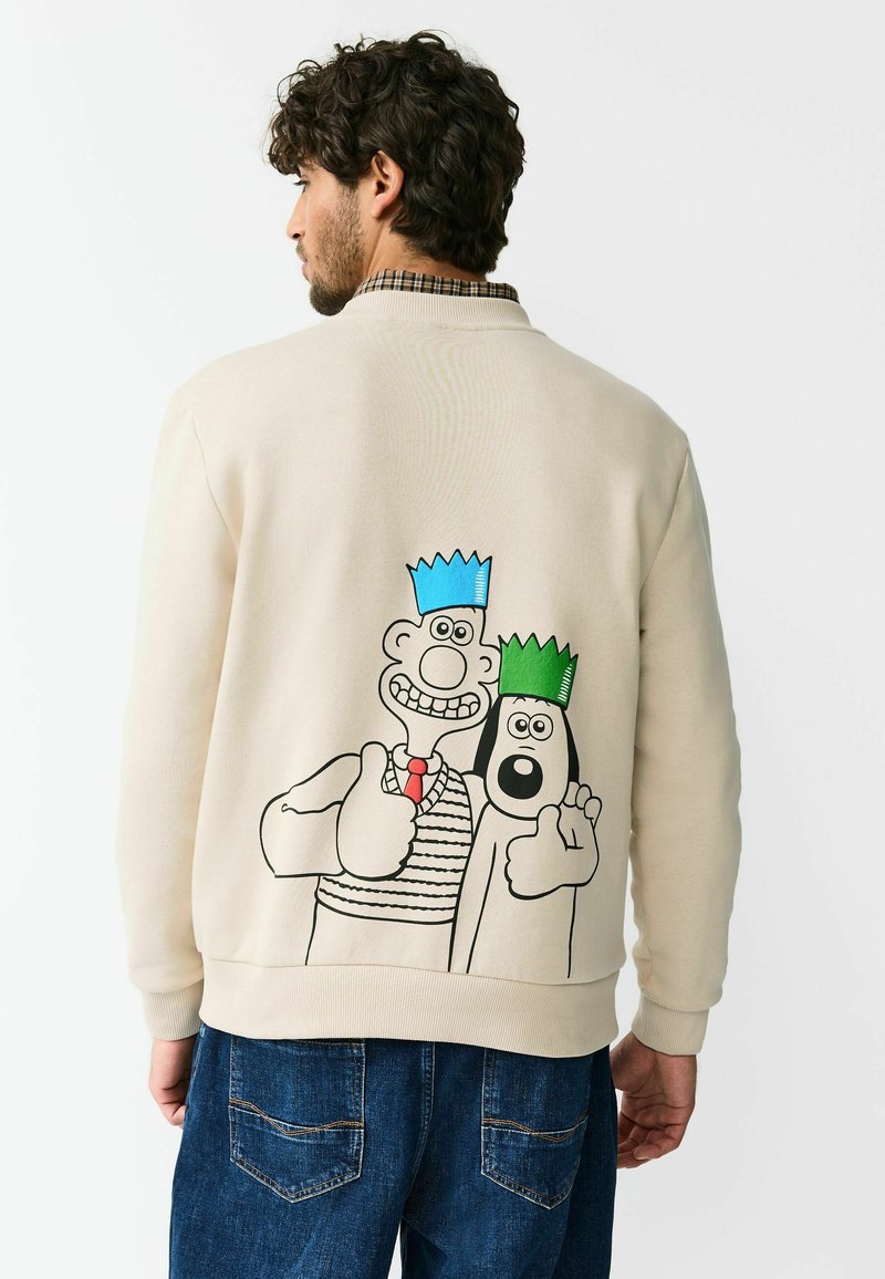 Beiger Pullover mit gerippten Bündchen an Ärmeln und Saum, mit einer Cartoon-Grafik von zwei Charakteren mit bunten Kronen auf der Rückseite.