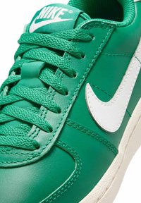 Zielone skórzane sneakersy z białym logo Swoosh, teksturowanymi sznurowadłami, przeszyciami oraz teksturowaną białą podeszwą.