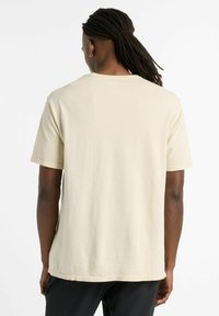Short-sleeve, light beige T-shirt made of textured fabric with a relaxed fit, featuring a round neckline and a straight hem.