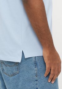 Lyseblå polo med tekstureret finish, sideventiler og korte ærmer, sat sammen med lyseblå denimshorts.
