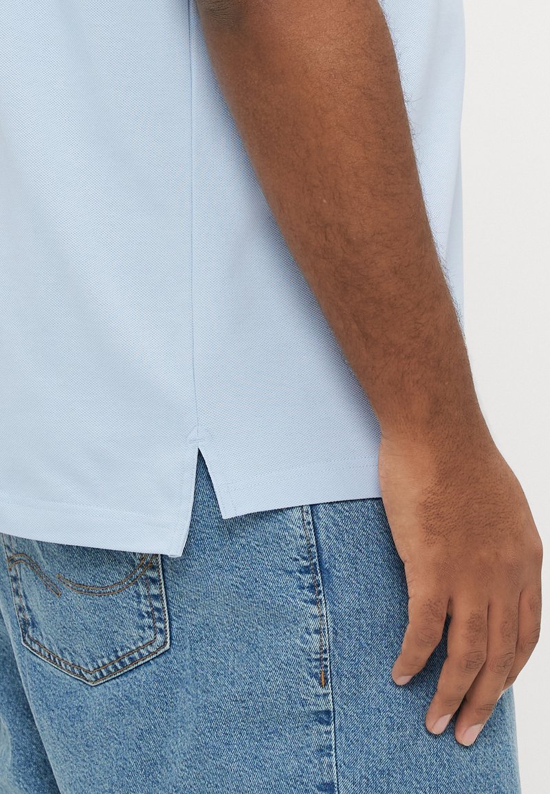 Light blue polo shirt with a textured finish, side vents, and short sleeves, paired with light blue denim shorts.