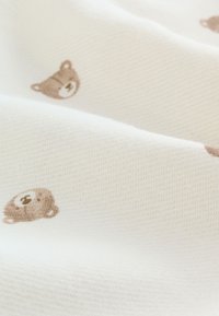 Tissu blanc à surface texturée présentant un motif dispersé de petits visages d'ours marron clair.