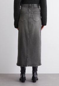 Gray denim midi skirt with a straight shape, back pockets, and a centered seam. Worn with black knee-high boots.