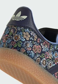 Floral patterned sneaker with a navy textile upper, rubber sole, and a grey accent logo on the heel. Features pastel-colored embroidered flowers.