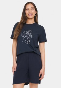 Mörkblå bomull t-shirt med korta ärmar som har en vit konturdesign av en hund som bär glasögon och texten "bonjour". Matchas med matchande shorts.