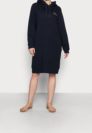 Donkerblauwe hoodie-jurk gemaakt van zachte stof, met een voorzak in kangaroestijl, geribde zoom en gouden accenten in borduurwerk op de borst.