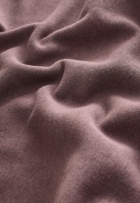 Mekana, teksturirana tkanina u prigušenoj boji ružičasto-ljubičaste, s finim pletenim uzorkom i nježnim nabiranjem, prikazujući nabore i konture.