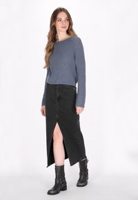 Grauer Strickpullover mit strukturiertem Finish, kombiniert mit einem schwarzen Jeansmaxirock mit einem Schlitz vorne und schwarzen Stiefeletten mit Schnallen.