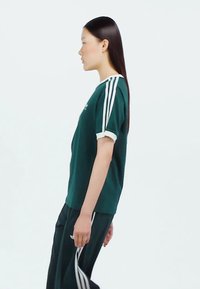 Green sports shirt with white accent sleeves, paired with black pants featuring white stripes. Simple, classic athletic design.