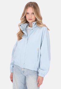 Vaaleansininen tuulitakki, jossa on korkea kaulus, joustavat hihansuut ja rento istuvuus. Takissa on painonapit ja hienovarainen logotunnus.