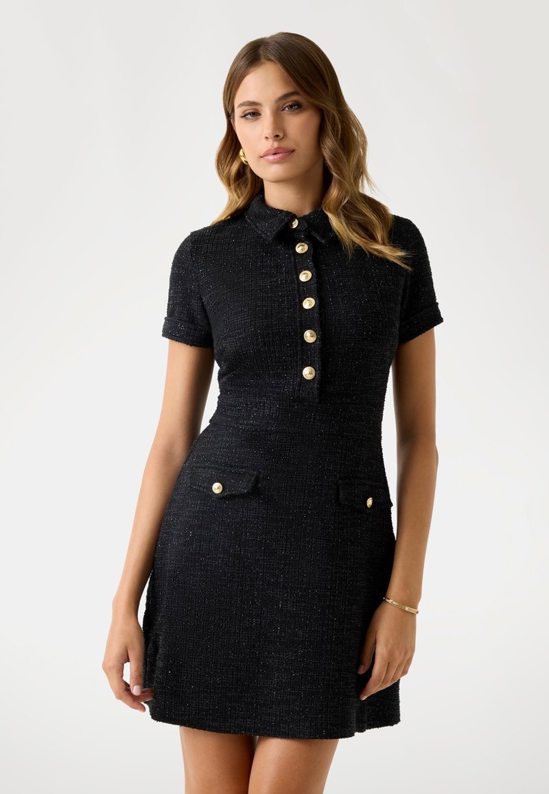 Robe noire texturée avec des manches courtes, un col, des boutons dorés sur le devant et des poches latérales. Elle possède une taille cintrée et une jupe évasée.