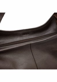 Intérieur d'un sac à main en cuir marron avec une poche zippée. Surface texturée, couture lisse et logo de marque en relief visible.