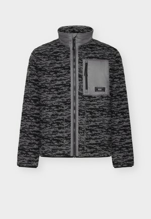 Veste en polaire noire et grise avec fermeture éclair à l'avant, col haut et une poche poitrine. Présente un motif texturé et des poignets côtelés.