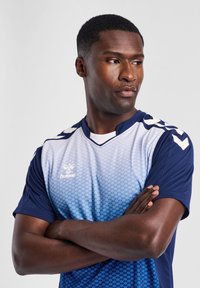Blauw en witte sporttrui met korte mouwen en een geometrisch patroon, voorzien van een V-halsontwerp en logo op de borst.