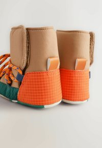 Braune Stiefel mit orangen strukturierten Akzenten, blauen und orangefarbenen Schnürsenkeln, grünem Stoff an der Unterseite und weißen Gummisohlen.