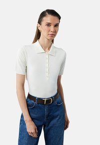 Hvid polo-shirt med korte ærmer, slim fit, med knaplukning og krave, parret med højtaljede blå denim jeans.