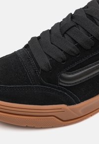 Baskets en daim noir avec de grosses lacets noirs, une semelle en caoutchouc gomme texturée et un détail de bande latérale noire rembourrée.