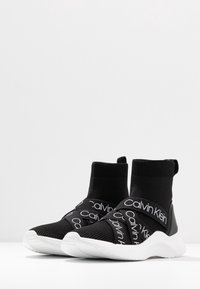 Černé pletené tenisky s vysokým střihěm, kontrastní bílou podrážkou a elastickými pásky s logem Calvin Klein.