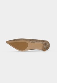 Chaussure à talon haut pointu à motif marron clair, vue du dessous sur un fond blanc uni.