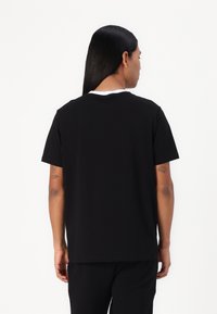 Svart t-shirt med kort ärm i bomull, med rund halsringning och vit kant. Avslappnad passform och slät textur, enkel design.