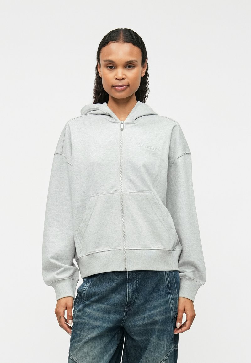 Γκρι φούτερ με φερμουάρ και χαλαρή εφαρμογή, κουκούλα με κορδόνι, μπροστινές τσέπες και κεντημένο λογότυπο στο στήθος. Μαλακό υλικό βαμβακιού.