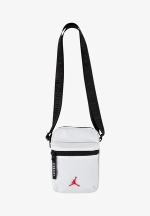 Bolso bandolero blanco con correa negra, que cuenta con un bolsillo frontal con cremallera y el logo de Jordan en rojo. El material parece duradero y tiene una textura suave.
