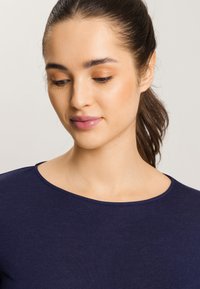 Top blu navy con scollatura rotonda, realizzato in tessuto morbido e elasticizzato. Texture liscia con dettagli minimi, focalizzandosi su una silhouette aderente.
