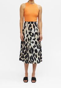 Débardeur orange rayé, jupe midi imprimé léopard noir et crème, tissu fluide, associée à des sandales à glissière noires, design minimaliste.