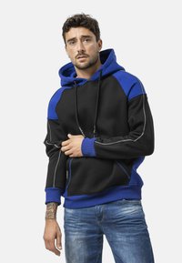 Sweat à capuche en tissu noir avec accents bleus, coutures contrastantes et poignets côtelés. Poche avant et capuche avec cordon incluses.