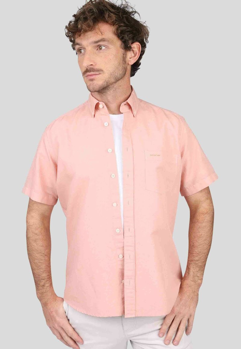 Chemise à manches courtes en tissu rose clair avec un col boutonné, une poche poitrine et un design uni. Ourlet légèrement incurvé et boutons visibles.