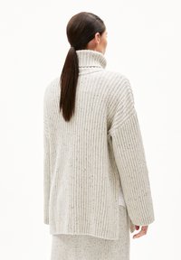 Hellgrauer Strickpullover mit hohem Kragen, gerippter Textur, lockerer Passform und Seitenschlitzen. Modell von hinten mit langen Haaren gezeigt.