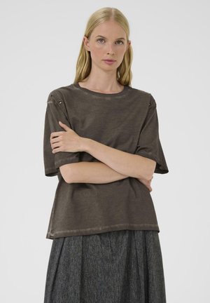 Brun, løstsiddende t-shirt med rund halsudskæring og korte ærmer, med skulderøskner, båret sammen med en struktureret, mørk nederdel.