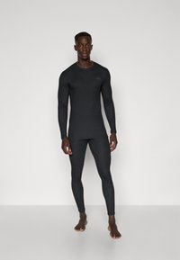 Completo attivo termico nero composto da una maglia a maniche lunghe e leggings aderenti, realizzati in un tessuto morbido con un sottile logo sul petto.