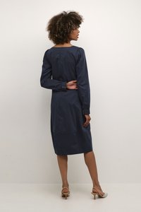 Tumedat sinine kleit pikkade varrukatega, ruudukujulise dekolteega, nööpidega mansettide ja sirge siluetiga, valmistatud sileda kangaga.