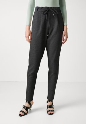 Pantalons de jogging gris foncé avec un motif texturé, taille élastique, cordon de serrage ajustable et coupe fuselée, associés à des sandales à talons avec lanières noires.