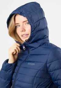 Giacca imbottita blu navy con cappuccio, caratterizzata da un design a quadri, zip frontale e logo sul petto. Il materiale sembra liscio e lucido.