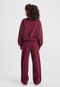 Burgundivärinen sweat set, jossa on löysä pullover puffihihalla ja leveät housut, valmistettu pehmeästä, teksturoidusta kankaasta.