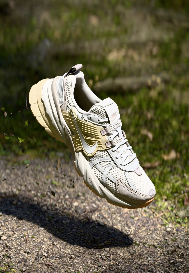 Chaussure de sport beige et grise avec une tige en maille, des accents texturés, des détails réfléchissants et une semelle épaisse, sur fond naturel.