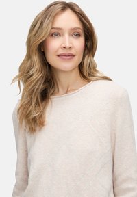 Jasno-beżowy sweter z miękkiego materiału, z chabrowym wzorem w diamenty i małymi cekinami, okrągłym dekoltem i długimi rękawami.