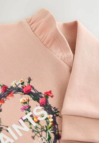 Ružová mikina s výšivkou kvetinového vzoru v rôznych farbách, s rebrovaným golierom a manžetami. Mäkká, hladká textúra.